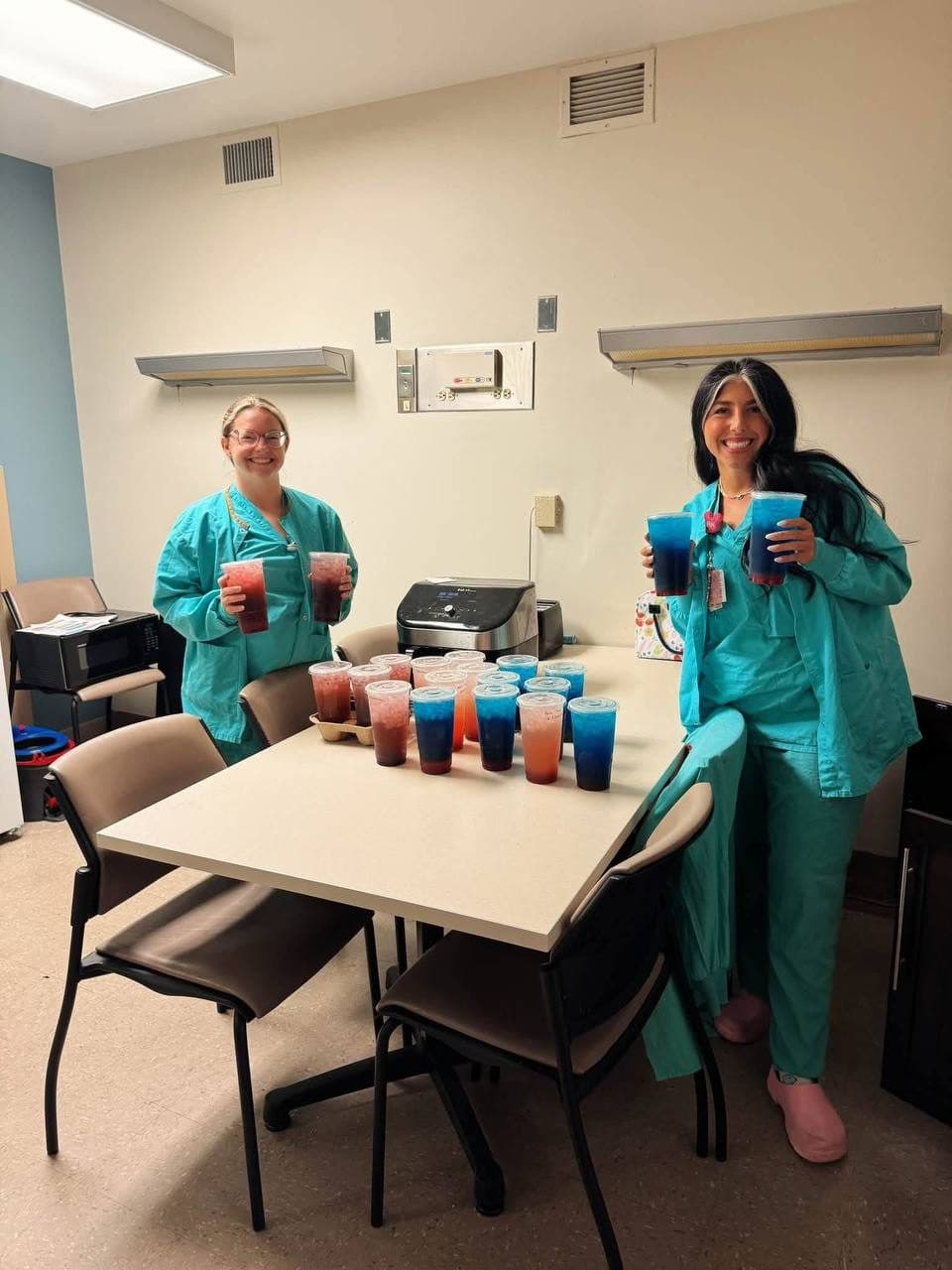 Two nurses in scrubs smiling with a big Flourish tea delivery in their break room