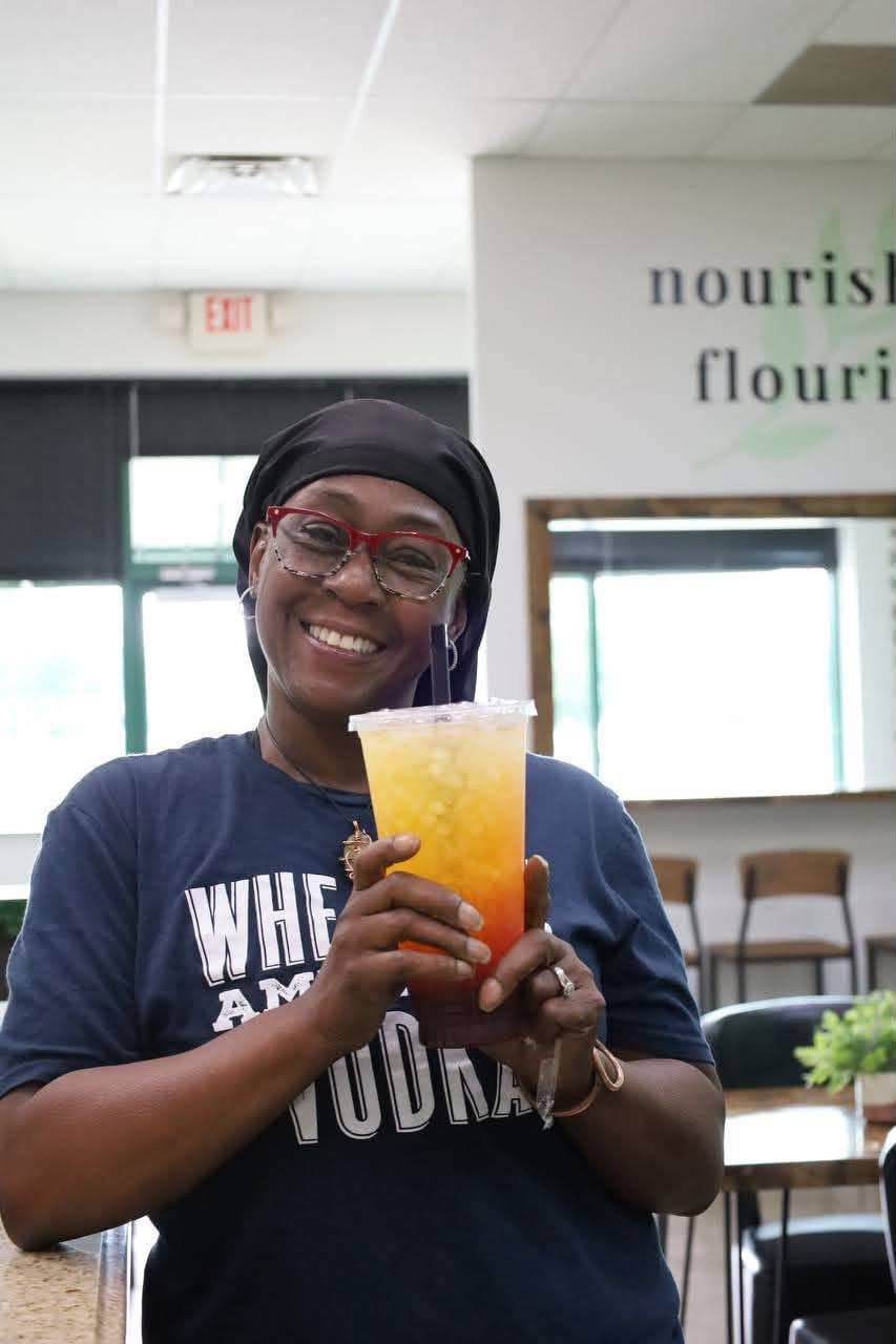 A beaming guest holding a sunrise ombre tea under the nourish and flourish wall