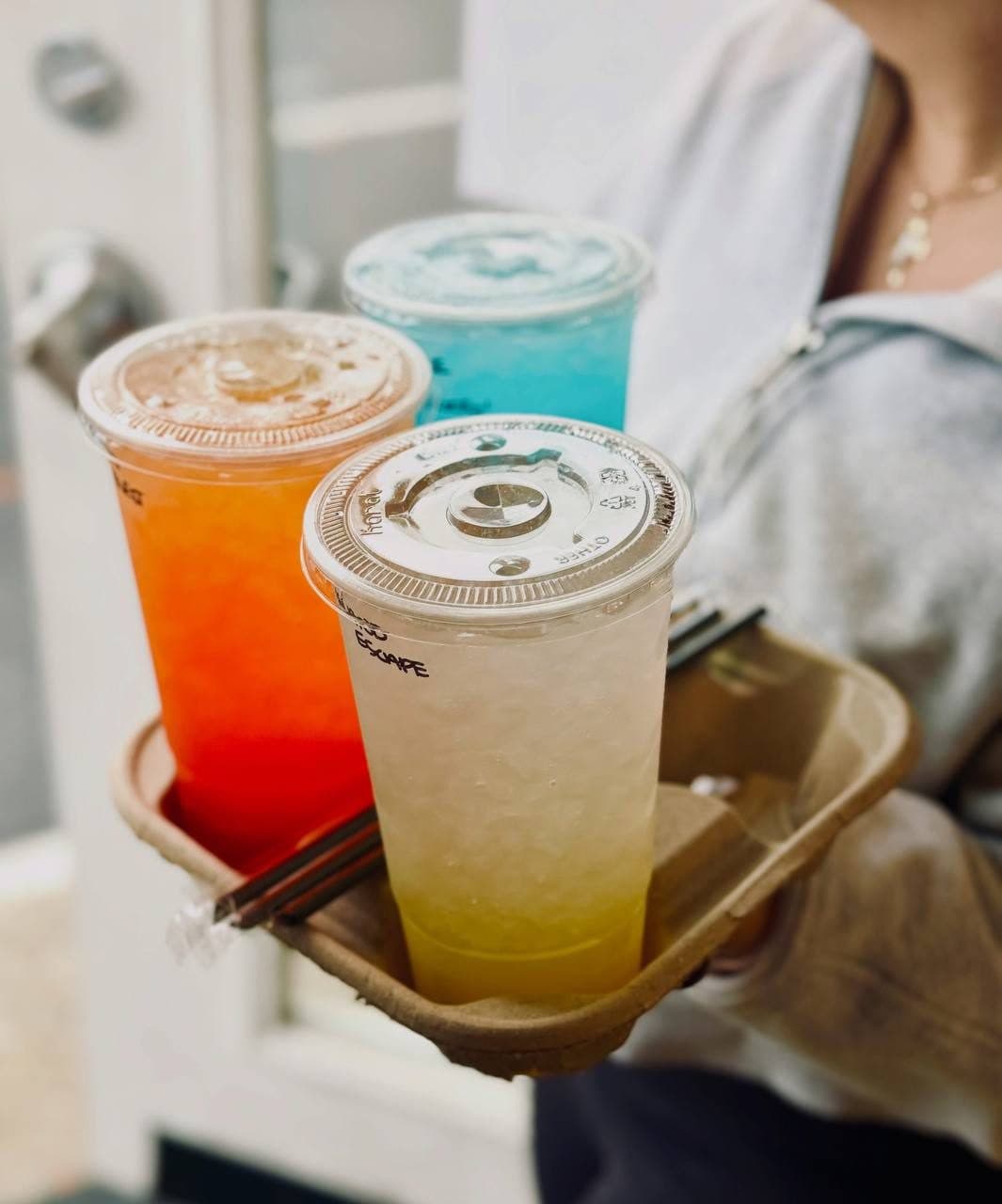 A to-go carrier with three colorful loaded teas held at the door